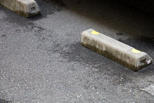 Concrete parking wheel stop on asphalt ground in a parking lot.