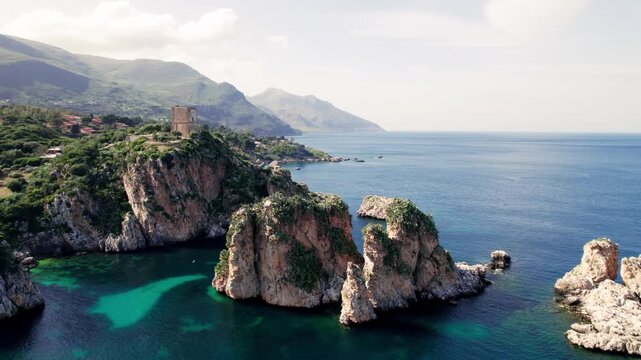 Aerial view of the Tonnara di Scopello cove, where emerald water meets limestone cliffs beneath a historic watchtower and the Faraglioni sea stacks.