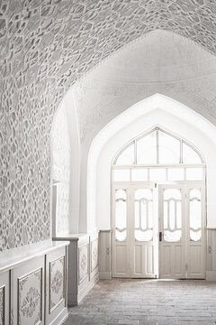 Ornate white plaster interior of Muhammad Amin Khan Madrasah in Khiva with geometric carved walls and pointed arch doorway. Ideal for travel publications, architectural features, cultural heritage.