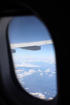 View looking through an airplane window showing the wing and fluffy white clouds