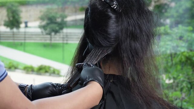 Close-up of red dye being brushed into a Southeast Asian woman's hair during a professional coloring treatment at a modern salon.