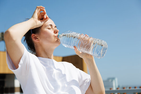 Woman drinking water during an extreme summer heatwave outdoors. Hydration, hot weather, high temperatures, heat safety, sun exposure and prevention of dehydration.