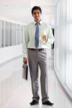 Businessman with bag and coffee cup standing in office corridor 