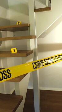 Yellow crime scene tape cordoning off a residential staircase with evidence markers placed on the wooden steps, indicating the location of clues during a forensic investigation at a murder site