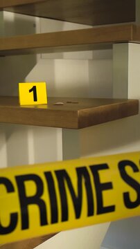 Yellow police tape reading Crime Scene sealing off a staircase inside a home, with an evidence marker and blood splatters on a wooden step, indicating a serious criminal investigation