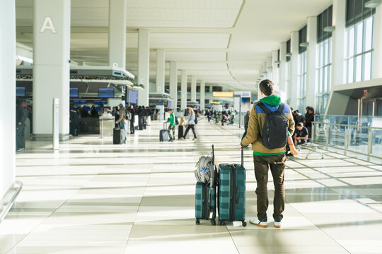 Father holding daughter and bags stands in a sunny airport terminal