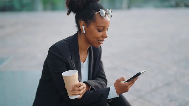 Mixed race woman resting in park, use smartphone, listen to music, drink coffee. Portrait of townswoman in recreation area in business district in city, phone addiction, modern mobile gadget overuse