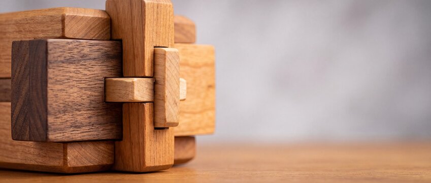 Wooden puzzle toy constructed from multiple blocks arranged in complex interlocking geometry on textured surface for brain game.