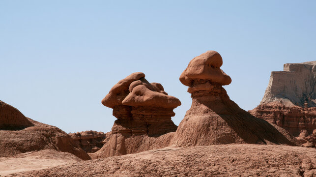Unique rock formations stand tall in a desert landscape in Utah. The sunlight reveals the shapes and colors of the rocks. The scene shows a clear blue sky above