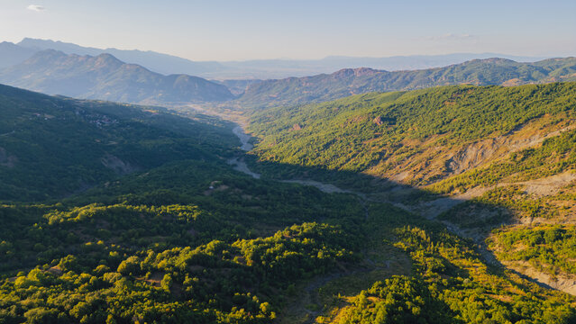 Panoramic aerial view of vast green mountain valley with river bed under warm sunset light in Thessaly Greece for nature landscape travel video background
