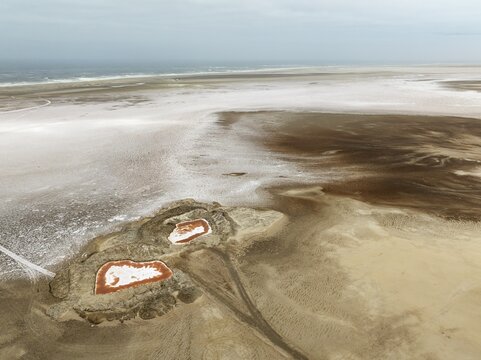 Saline ponds with ruddy algae growth and white salt deposits at the Atlantic Coast. Aerial view. Drone shot. Namib Desert, Skeleton Coast, Dorob National Park, Namibia