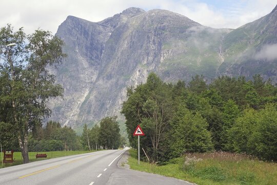 Empty country road surrounded by high mountains and green trees under cloudy sky, Raumadalen, Trollvegen, Andalsnes, Norway