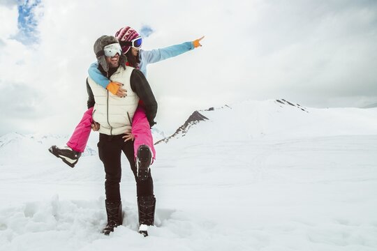 Joyful young couple walk piggyback in deep snow share romantic bonding on snowy mountain, symbolizing love, happiness, freedom, playful relationship, adventure, carefree winter escape, togetherness