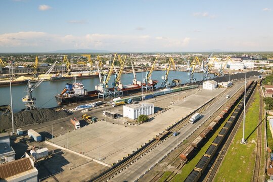 Poti, Georgia - 22nd august, 2025: aerial view Busy seaport with cranes, bulk piles, cargo ships, warehouses, rail tracks, bus on road, clear sky, logistics hub, Black Sea city Poti, Georgia, daytime