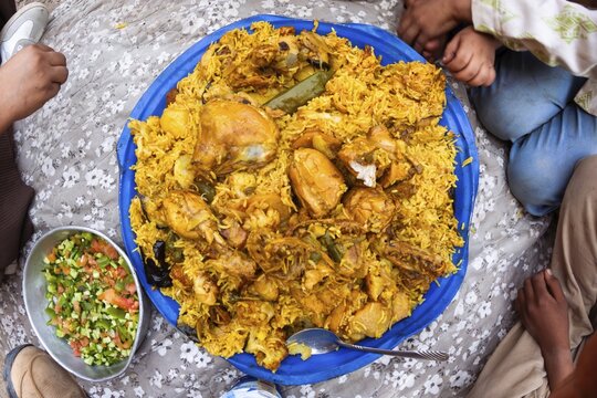 Shared handmade chicken rice platter with salad and yogurt communal dining hands eating traditional Middle East cuisine family gathering close up