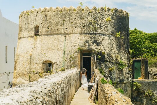 Woman tourist in white dress explores sightseeing the ramparts of the Old Fort in Stone Town, Zanzibar. Highlights include 17th-century Omani architecture and historic coral stone walls