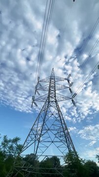 Close-up bottom view of electricity overhead power lines and utility poles silhouetted against a colorful sunset sky in Islamabad, Pakistan. Urban infrastructure, energy transmission, and power distri