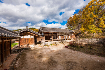 Fototapeta premium Traditional Korean Hanok House Featuring Wooden Structure, Stone Foundation, and Tiled Roof Set Against a Dynamic Blue Sky and White Clouds