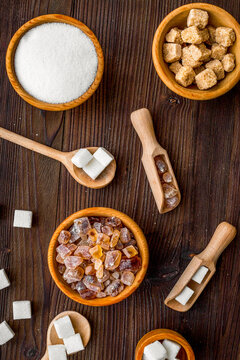 Sugar background on dark wooden table. Bowls with different kinds of sugar. Top view