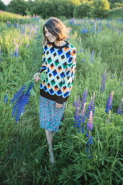 Smiling woman holds a lupine in a summer field