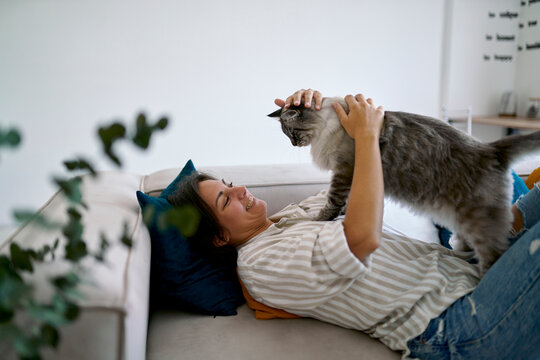 Happy woman stroking and playing with cat at home