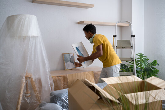 Man arranging decor and choosing frames while unpacking in home