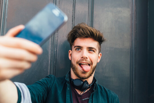 Portrait of young man pulling funny face taking selfie with smartphone