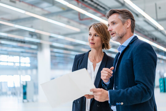 Businessman and businesswoman discussing plan in a factory hall