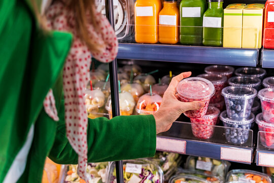Woman taking packaged berries from cooling shelf in organic store