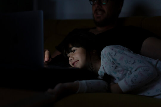 Smiling daughter and father looking at laptop on couch at night