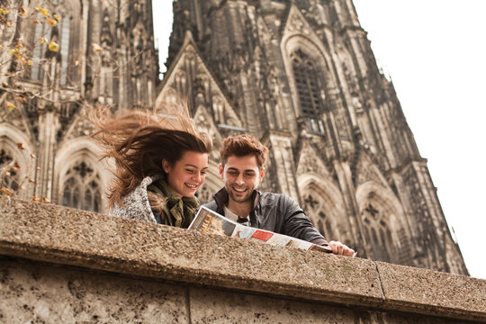 Germany, Cologne, young couple watching city map in front of Cologne Cathedral