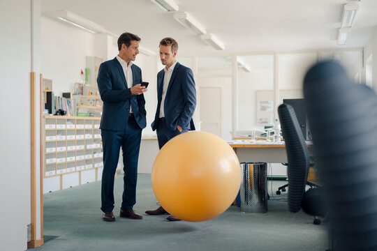 Two businessman checking smartphone with yellow fitness ball in foreground