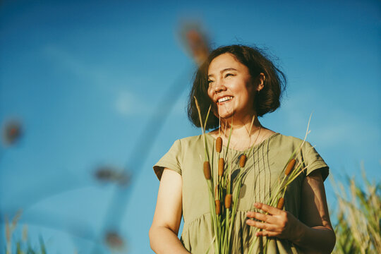 Happy woman holding bunch of reed grass in hand on sunny day