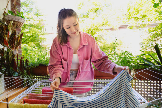 Woman hanging fresh laundry on a drying rack on a sunny balcony