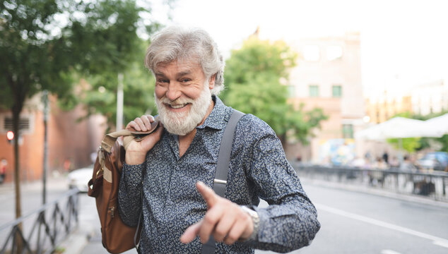 Happy white bearded mature man gesturing while carrying luggage