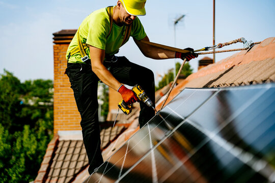 Engineer wearing hardhat using drill machine to install solar panel