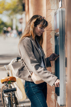 A woman uses a smartphone at a city atm to withdraw cash