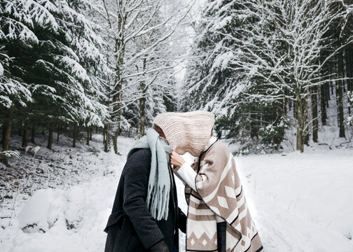 Romantic couple covering face with scarf while standing on snow in forest