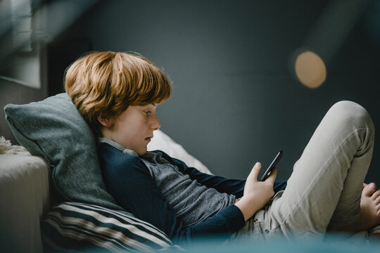 Redheaded boy lying on couch looking at cell phone