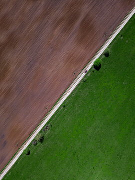 Aerial view of car driving along countryside road stretching between green and brown field