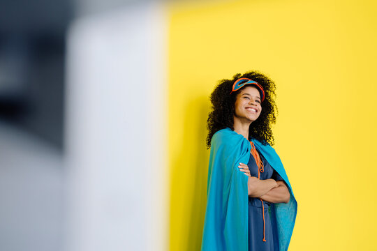Smiling woman in superhero costume looking away while standing in front of yellow wall