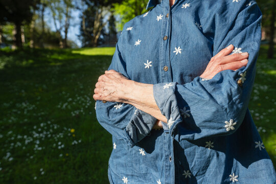 Retiree with crossed arms standing outdoors in sunny summer park