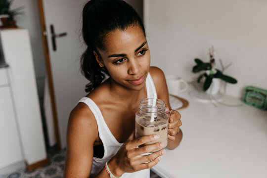 Portrait of young woman with glass of iced coffee in the kitchen