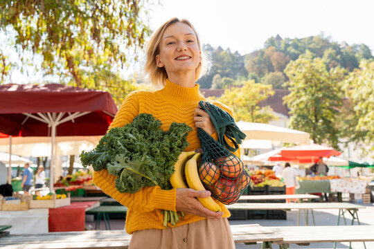 Smiling woman holding fresh and vegetables at farmer's market