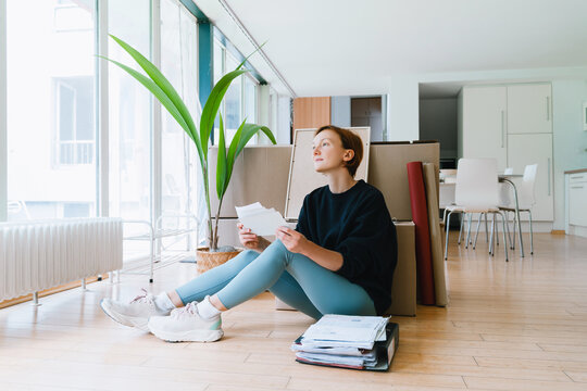 Woman sitting with paperwork in new apartment on moving day