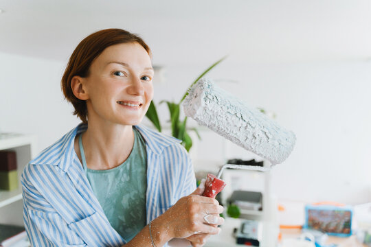 Smiling woman holds a paint roller during home renovation indoors