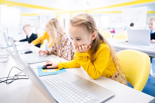 Blond schoolgirl learning through laptop in computer class