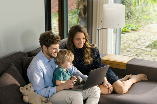 Smiling parents and son sitting on sofa using laptop at home