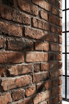 Closeup of exposed red brick wall texture in an industrial loft-style home office with warm afternoon light illuminating the rough surface