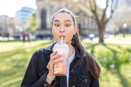 Young woman looking cross eyed while drinking milkshake at park